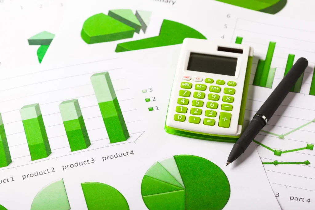 Vista completa de una calculadora con varios papeles con gráficos con la disminución de la huella de carbono para pymes.